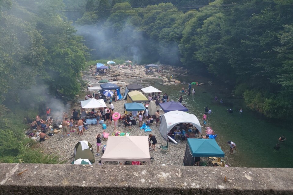 河川敷でBBQや川遊びを楽しむたくさんの観光客